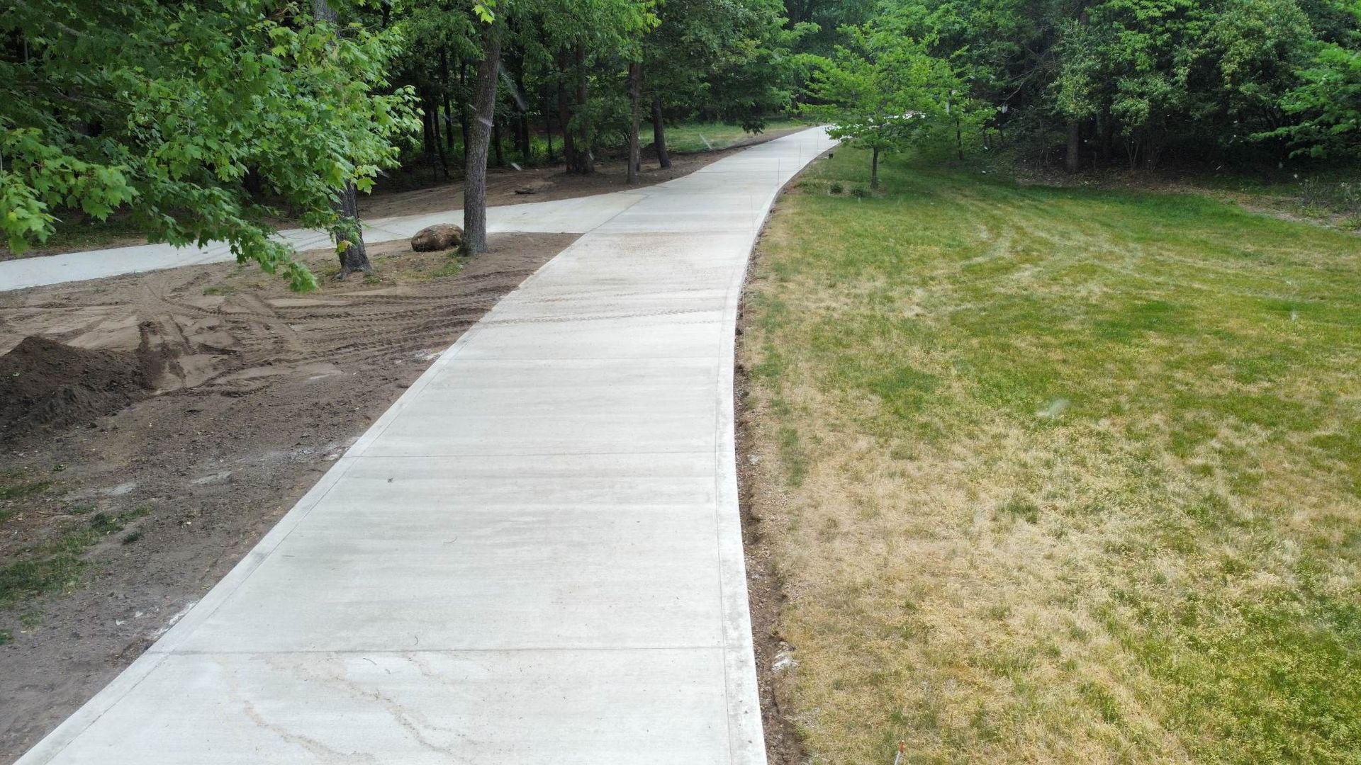 A concrete walkway going through a grassy field.
