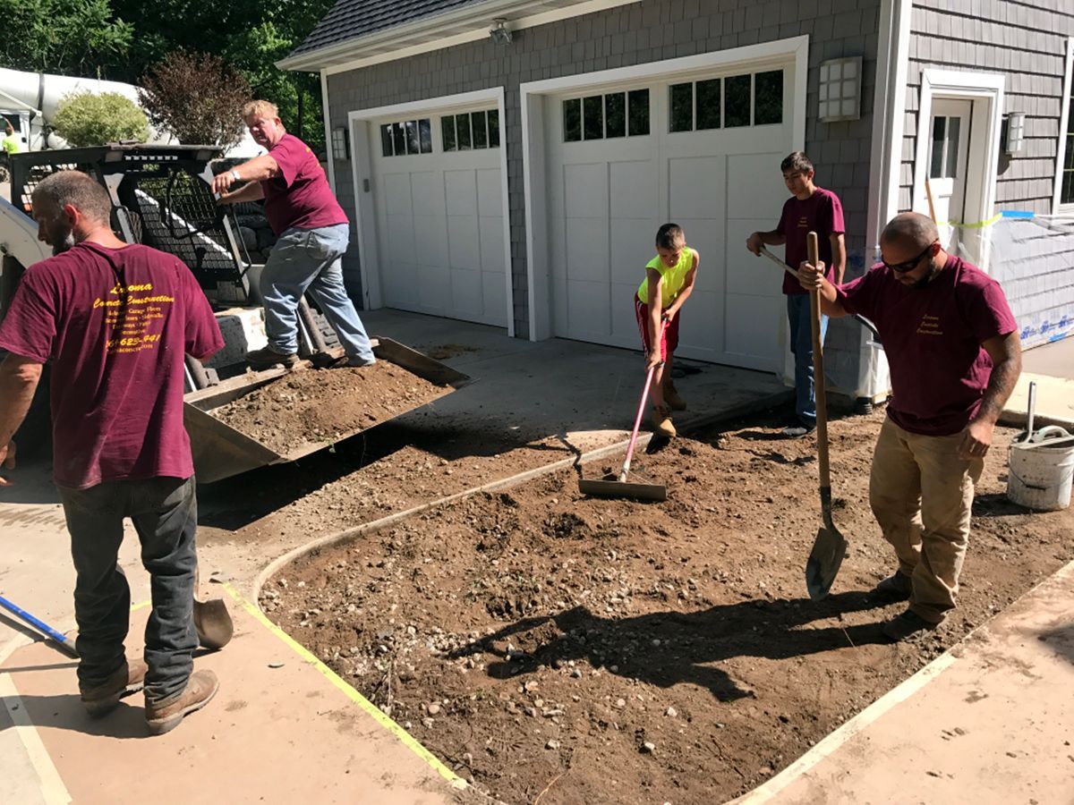 A group of men are working on a driveway in front of a garage.