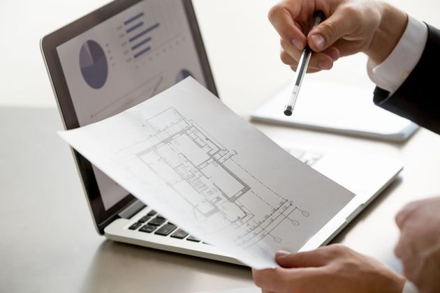 Hands reviewing a printed floor plan beside a laptop with charts on screen