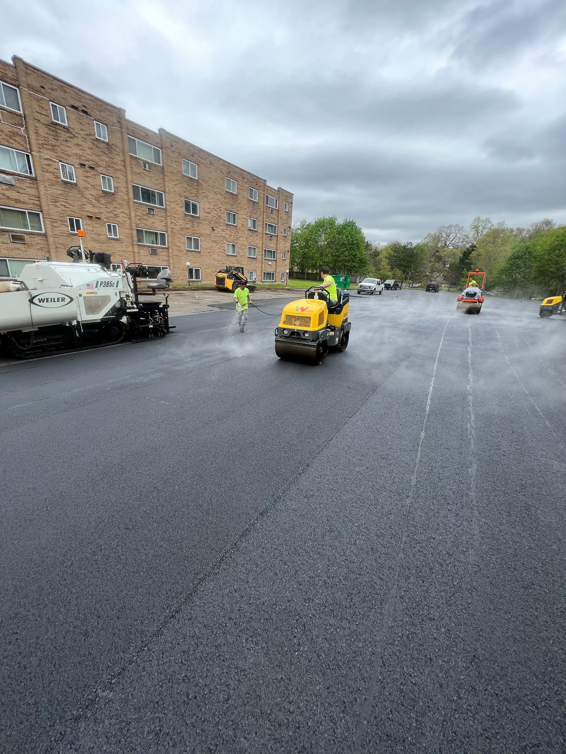 Rainy parking lot with brick apartments, utility trucks, and workers in high-visibility jackets