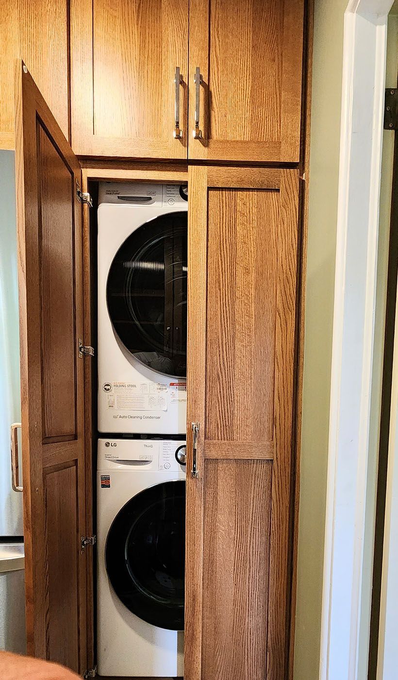 A washer and dryer are stacked on top of each other in a wooden cabinet