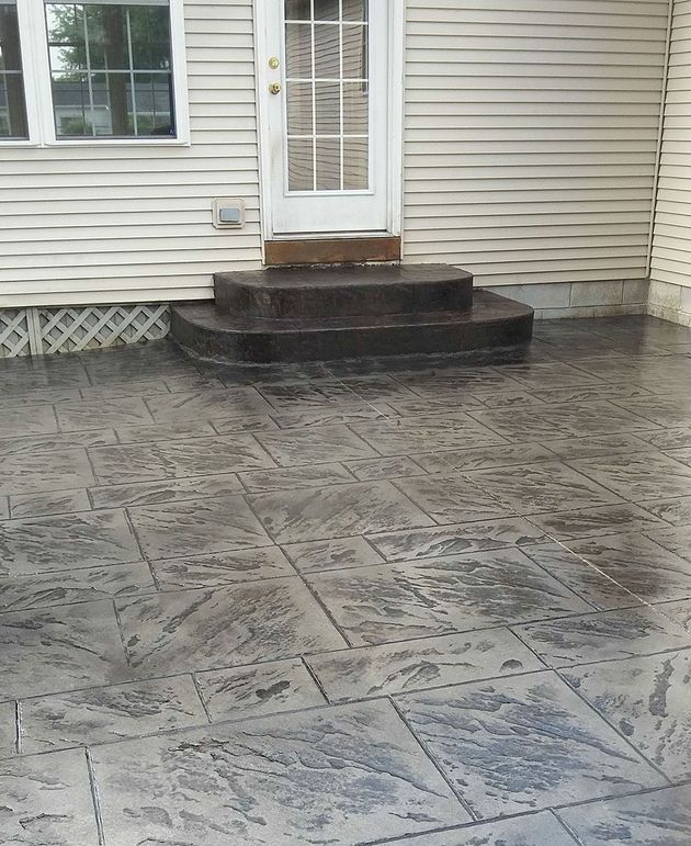 Wet stamped-concrete patio with a small front stoop and white door on beige siding