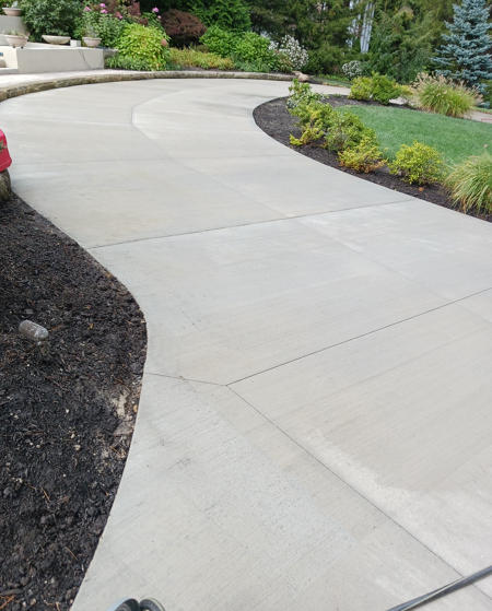 Curved concrete driveway bordered by landscaped garden beds and shrubs