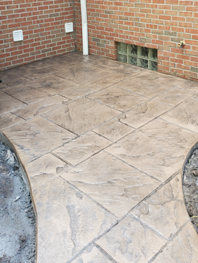 Stamped concrete patio beside a brick wall, with two white outlets and a small vent opening.