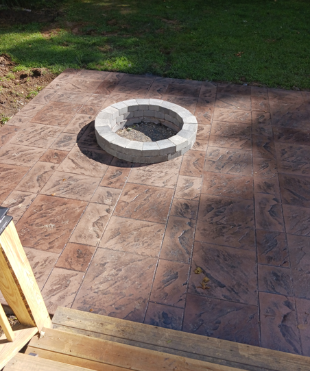 Stone fire pit on a tiled patio beside a grassy yard, viewed from a wooden step.