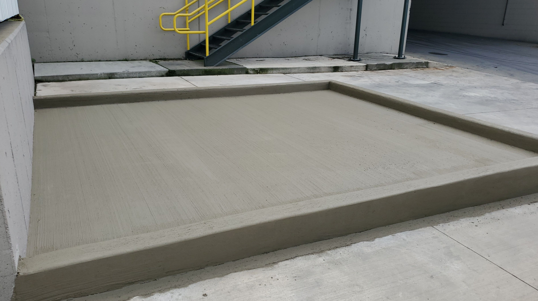 Concrete loading dock with a raised platform and yellow staircase beside a building