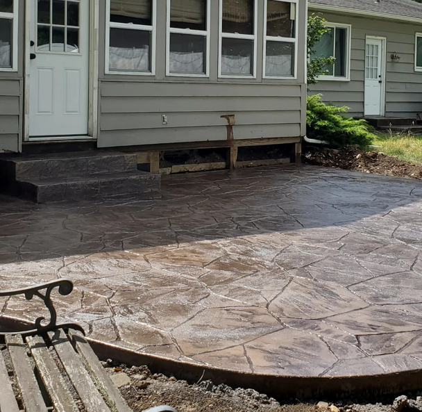 Stamped concrete patio and walkway beside a house with a porch and steps