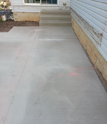 Concrete walkway beside a house, leading to steps and a side entrance.