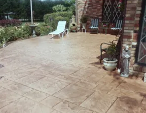 Stamped concrete patio with a white lounge chair, potted plants, and a brick house exterior.
