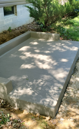Concrete wheelchair ramp beside a building, with low sidewalls and dappled tree shade