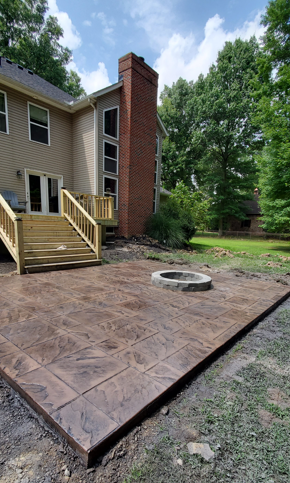 Stamped concrete patio beside tan house with wooden steps, brick chimney, and a circular fire pit.
