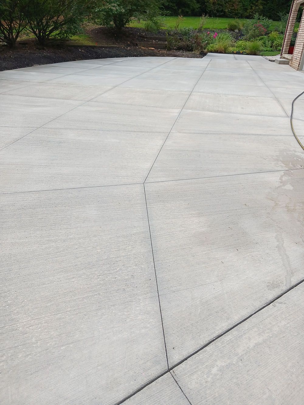 Concrete driveway with visible expansion joints leading to a grassy yard and brick house wall