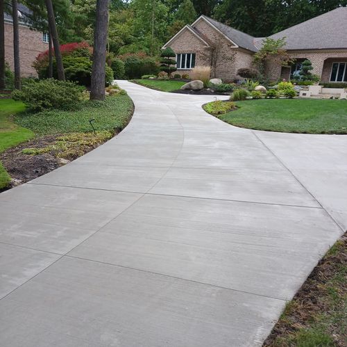 Curving concrete walkway leading to a stone house in a landscaped residential area