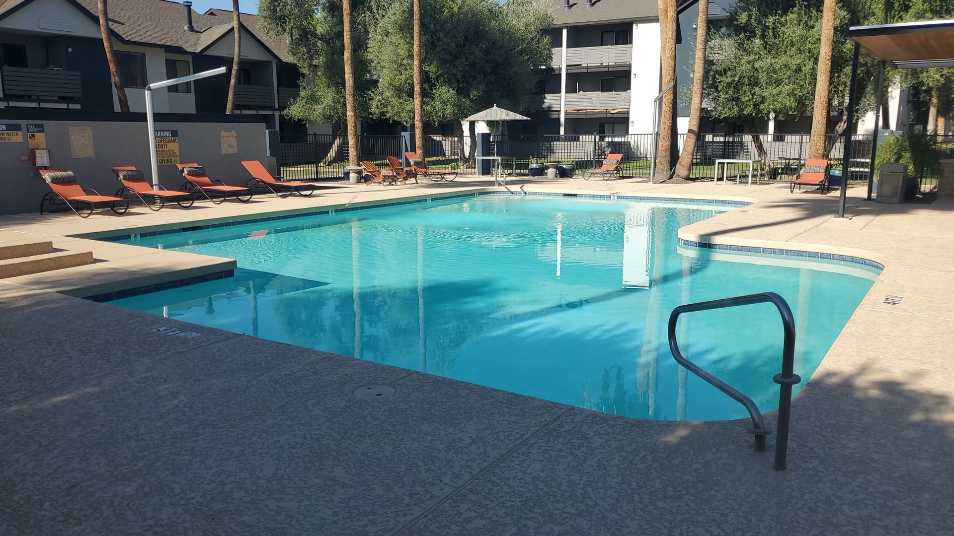 Outdoor apartment pool with turquoise water, lounge chairs, and a handrail in the foreground