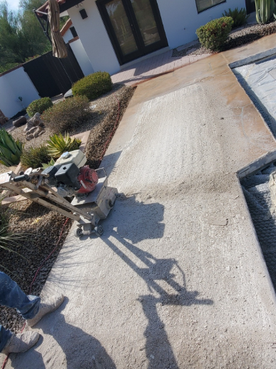 Person using a plate compactor on a light-colored walkway next to a pool.