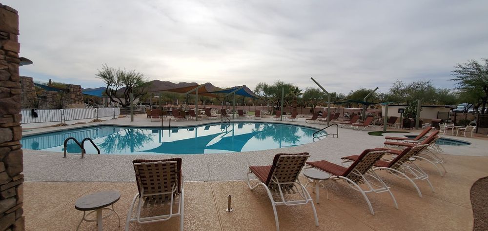 Swimming pool surrounded by lounge chairs, overcast sky, trees in the background.