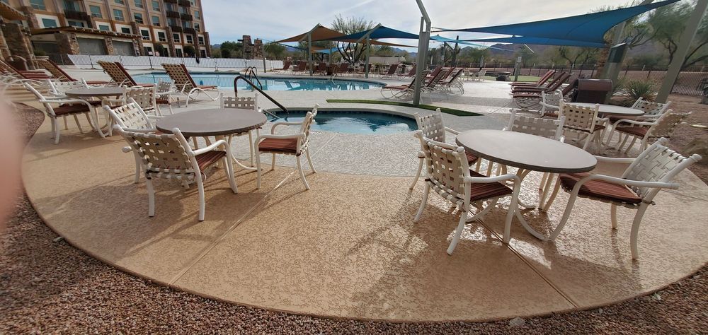 Poolside tables and chairs on a sunny day. A building and lounge chairs are in the background.