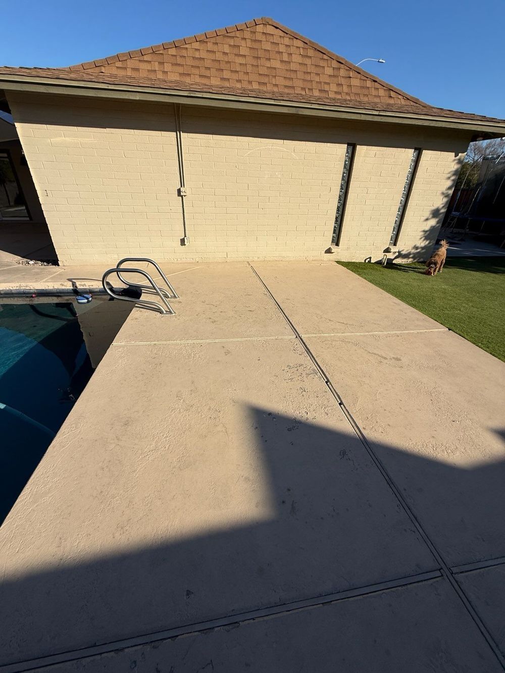Poolside patio with pool on left, house on right, clear sky.