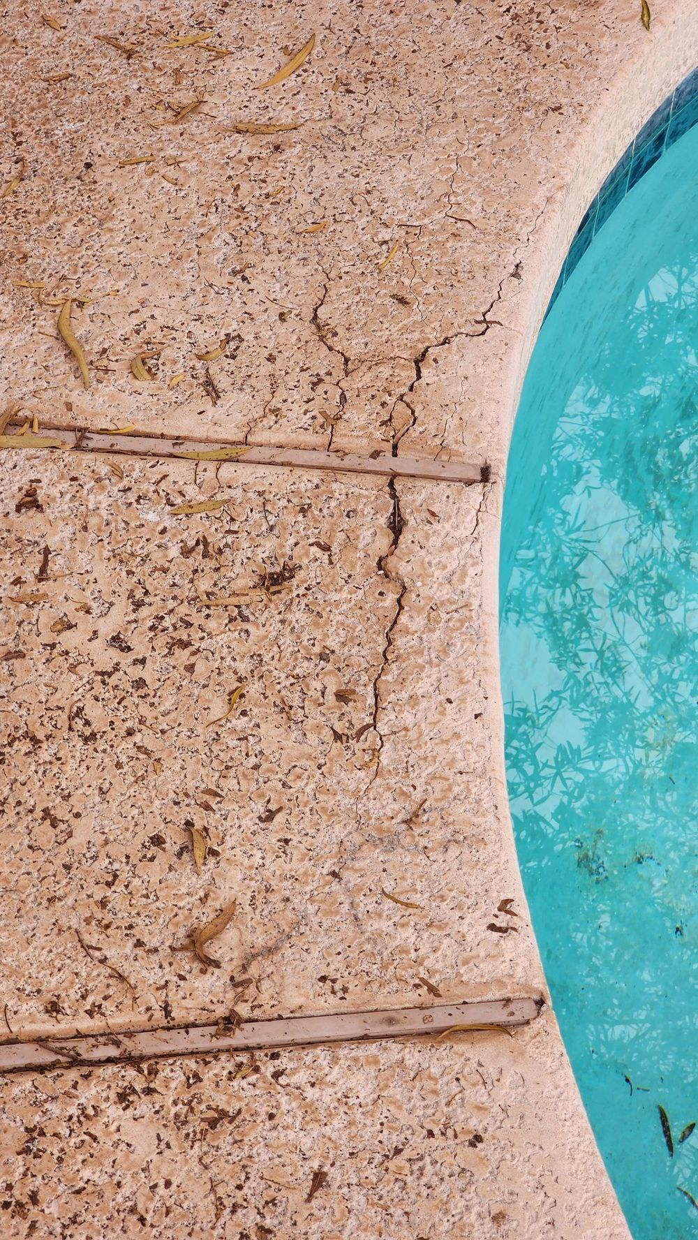 Cracked concrete pool deck next to turquoise pool water.