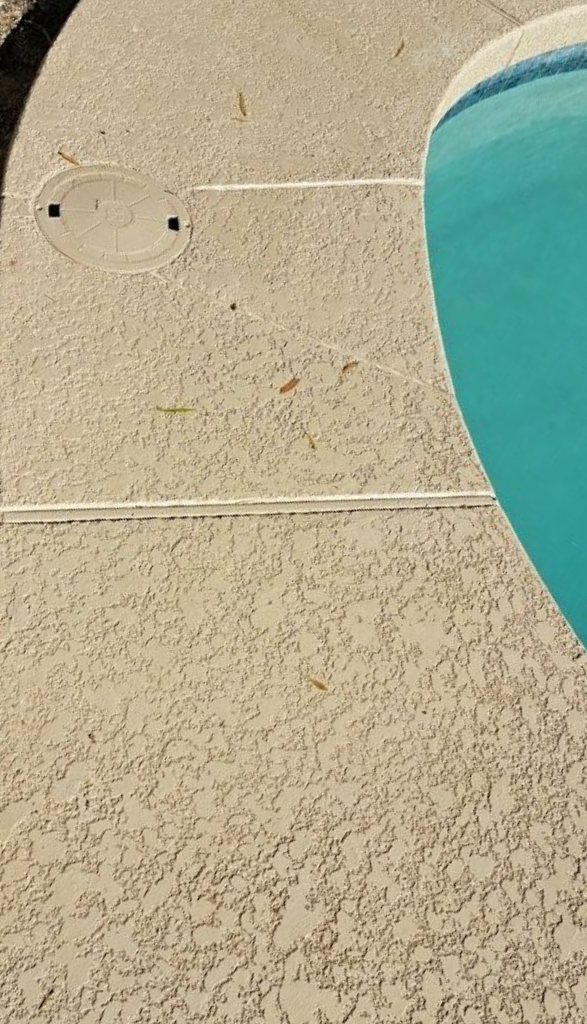 Curved concrete pool coping with textured surface, next to turquoise pool water.