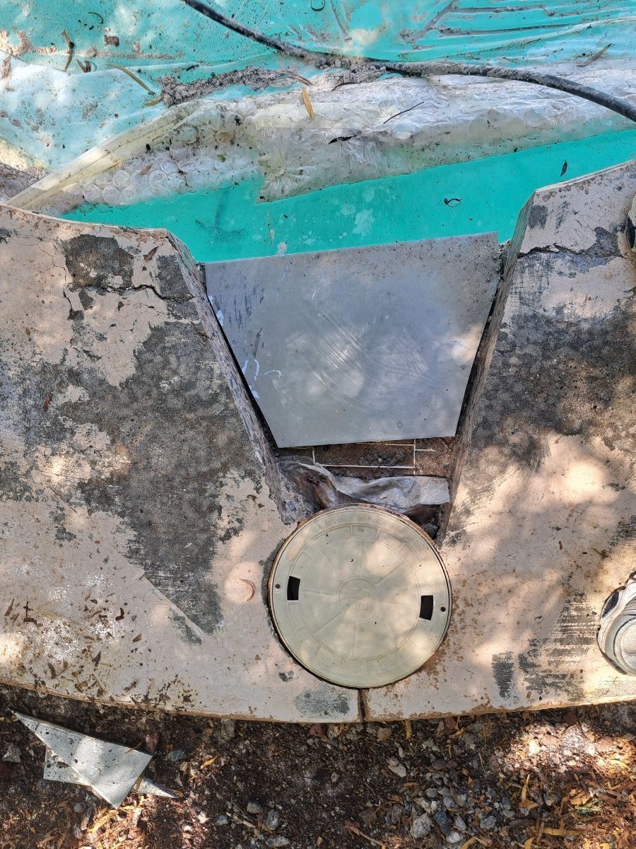 Top-down view of a swimming pool skimmer. Gray concrete, white cover, and turquoise water are visible.