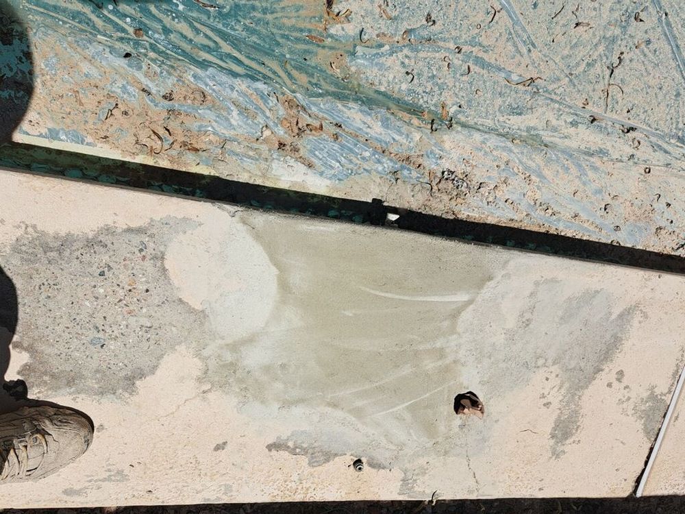 Patch of new concrete on a weathered surface with blue tarp visible in the background.