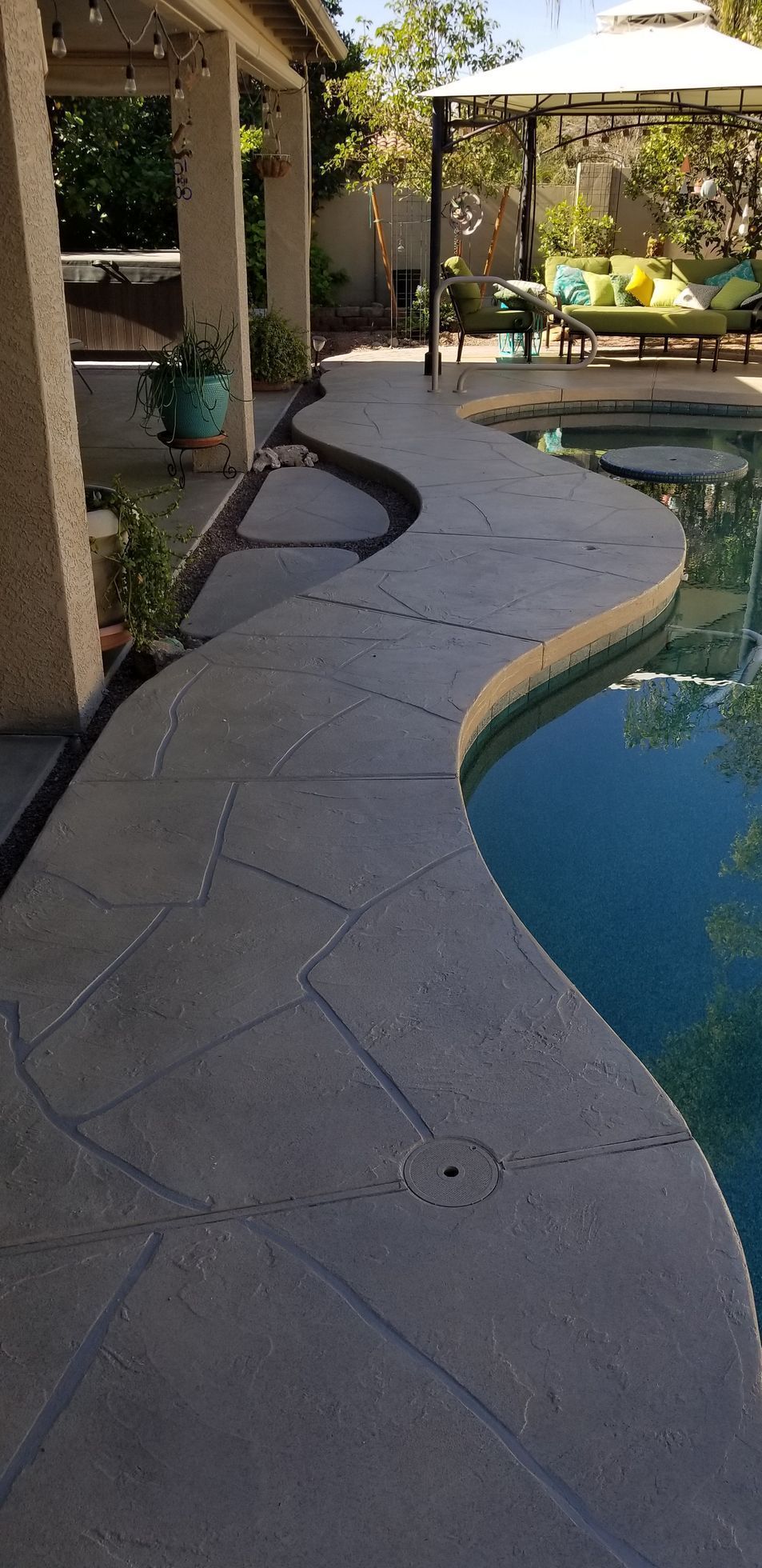 Curving concrete pool deck with water, a gazebo, and partial view of a covered patio.