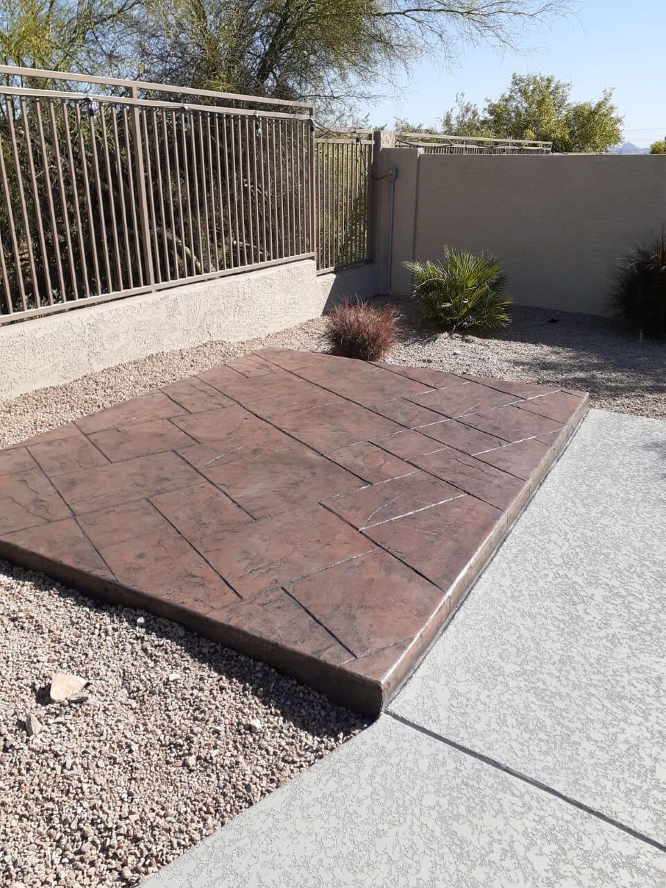 Brown stamped concrete patio with decorative lines, surrounded by gravel and a light gray concrete slab.
