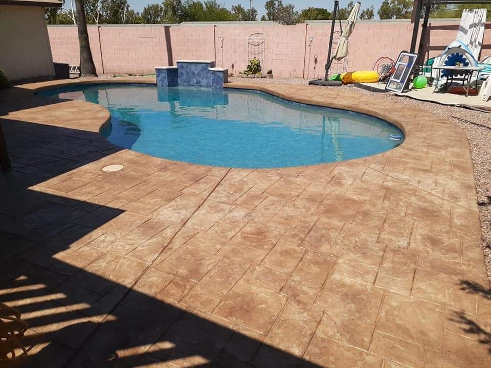 Pool with brown stamped concrete patio, blue water, and pink wall background.
