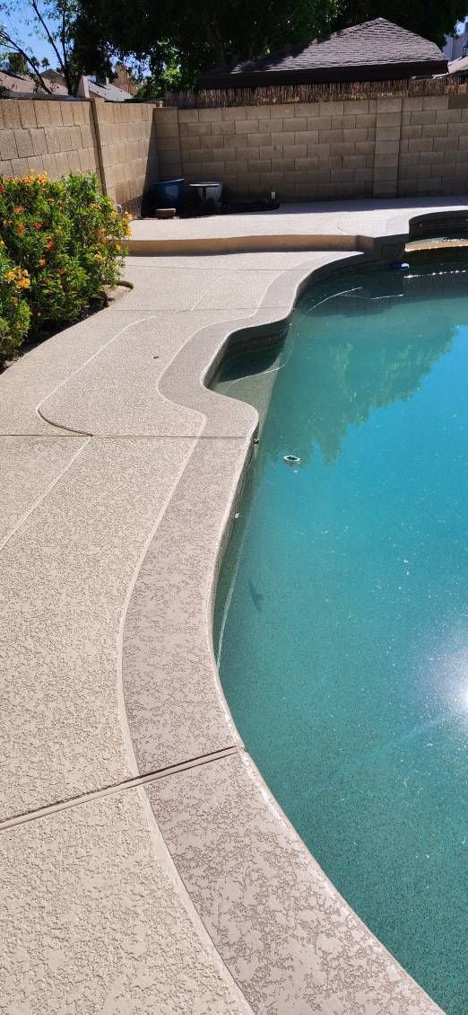 A swimming pool with turquoise water, a concrete edge, and a stone wall in the background.