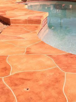 Stamped concrete patio in a brick-like pattern, bordering a pool with clear water.