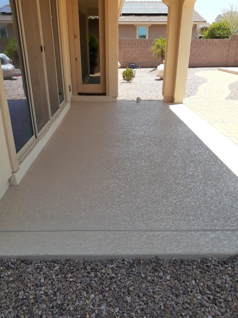 Covered patio with speckled concrete floor, beige walls, and a view of a gravel path.