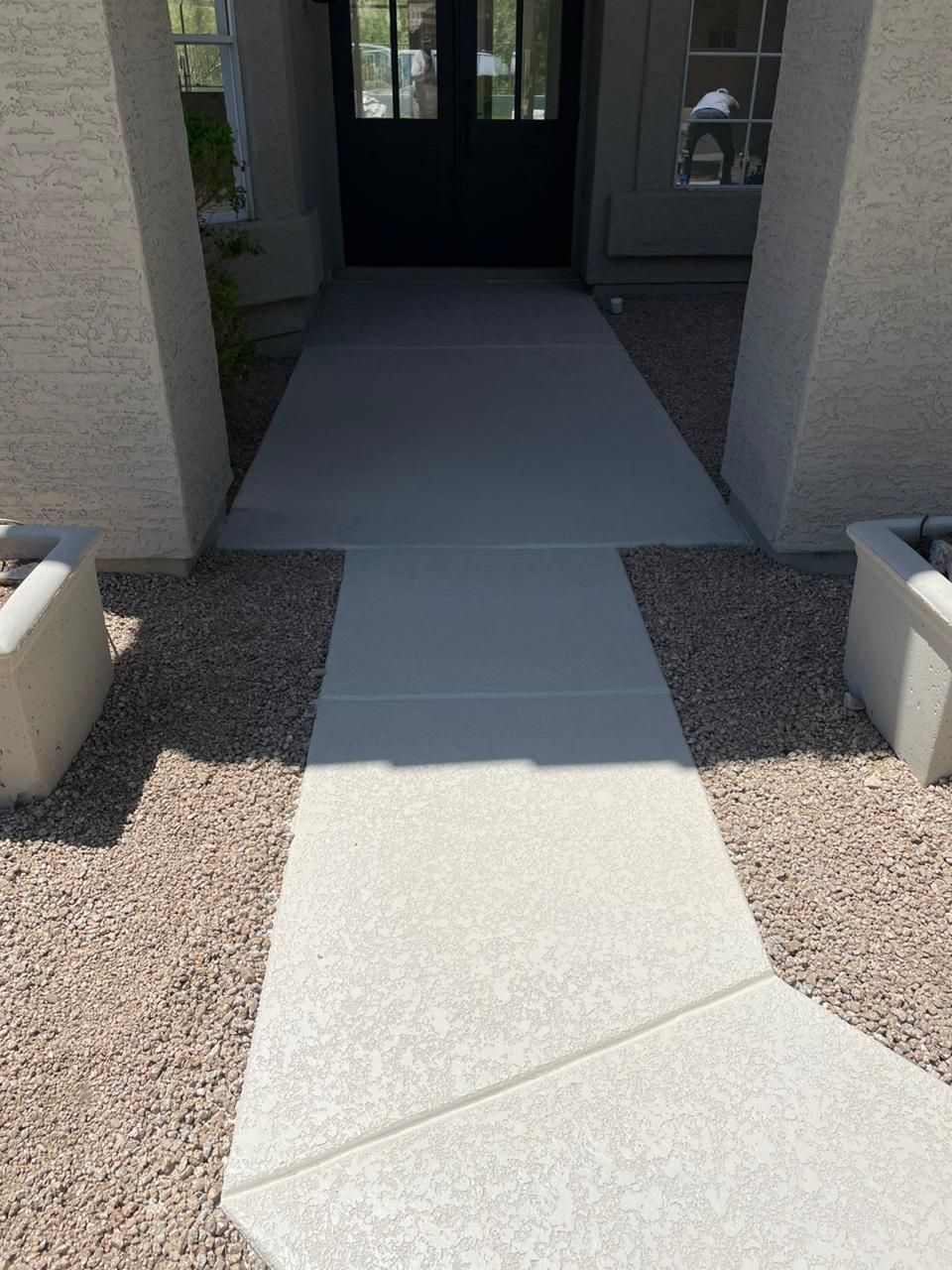 Concrete walkway leading to a black door, flanked by gravel and planters.