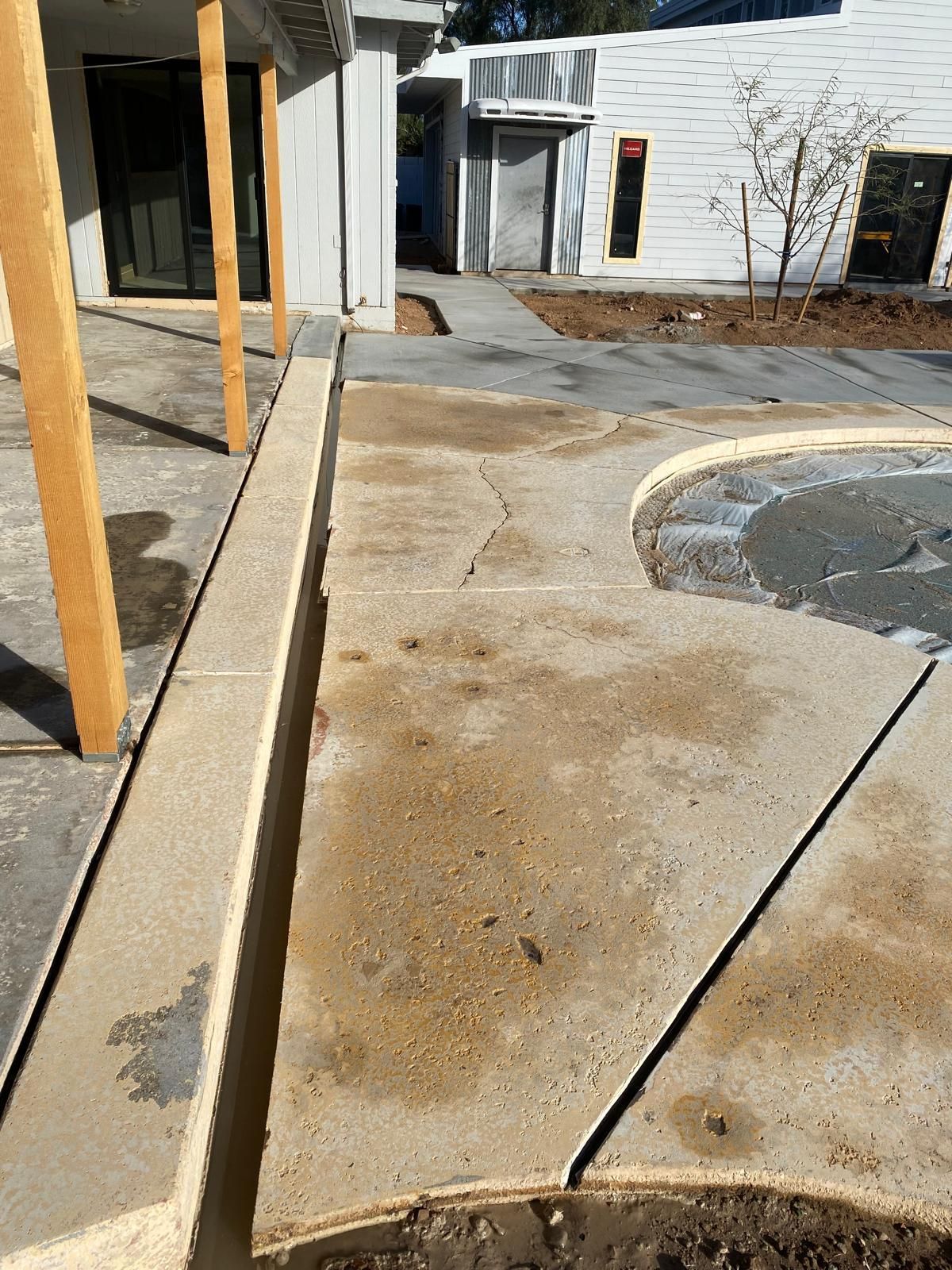 Concrete walkway with cracks and standing water, near a building with wooden support beams.