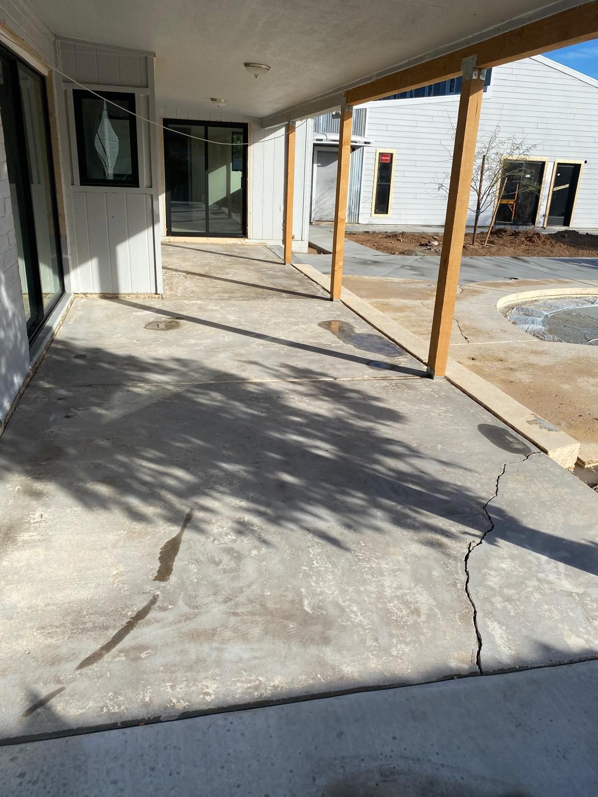 Concrete patio with shadows, cracked surface, and wooden supports.