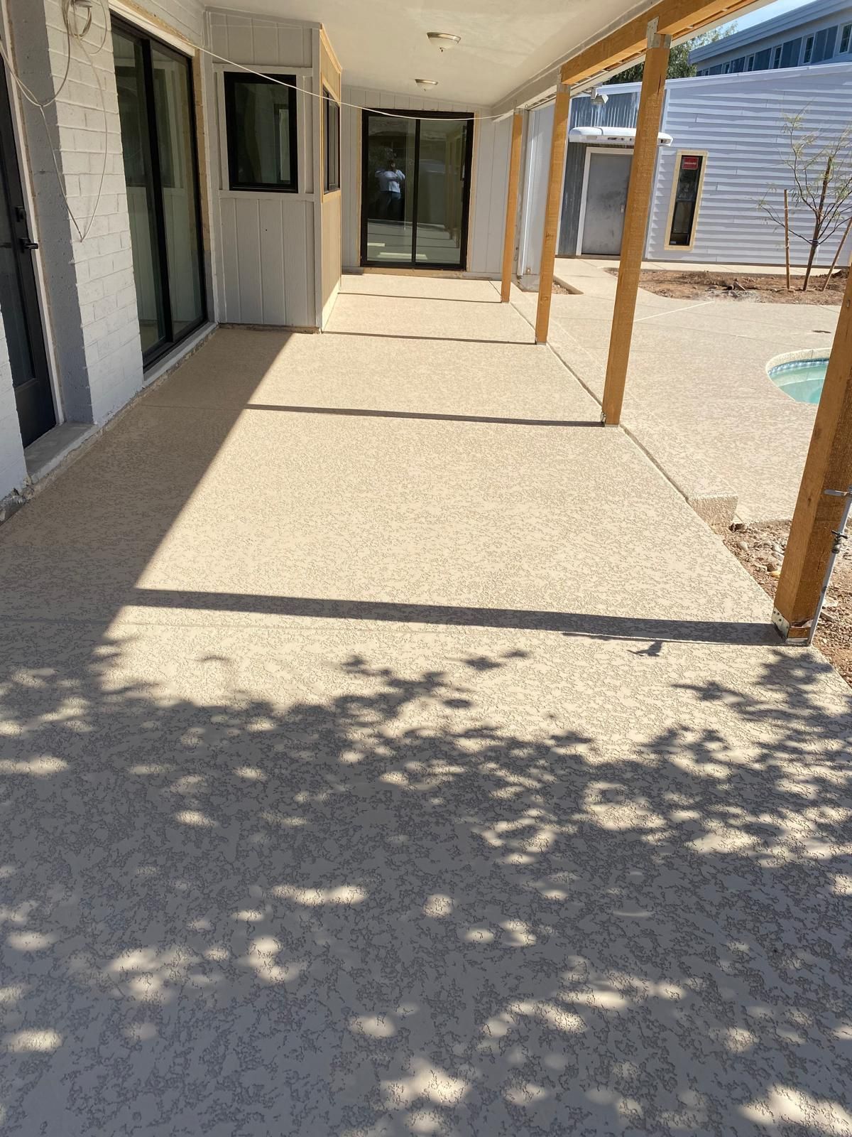 Covered walkway with exposed aggregate floor, wooden posts, and shadows.