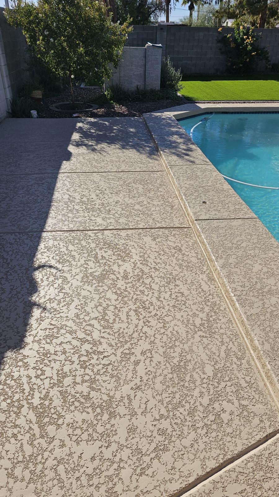 Concrete patio leading to a swimming pool, partially shaded.  The patio is textured, and the water is clear.