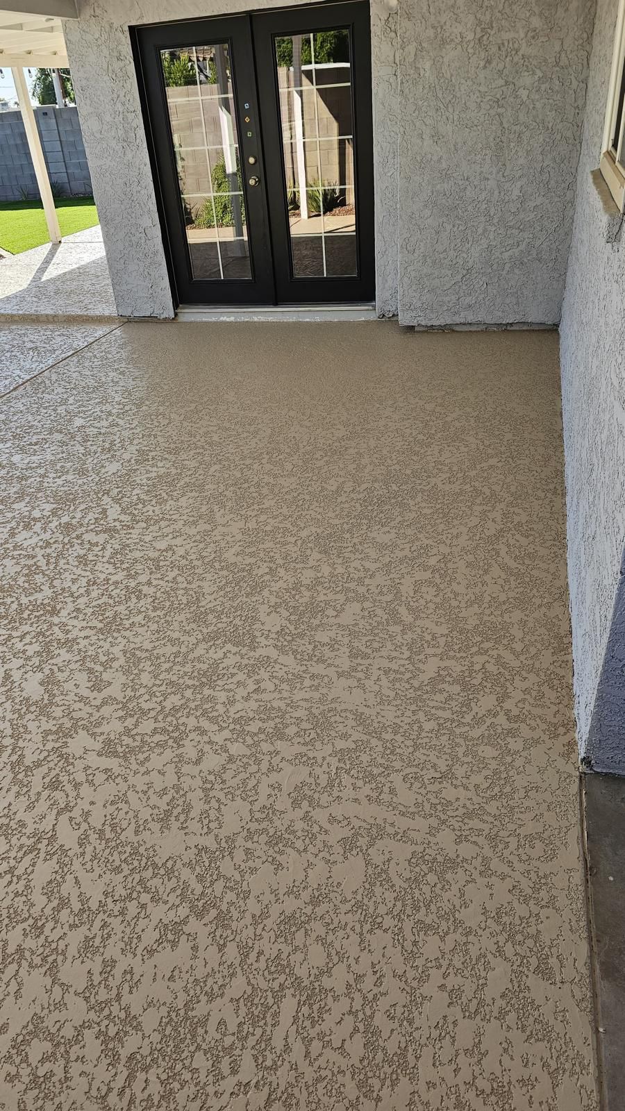 Tan textured concrete patio, double black doors, stucco walls.