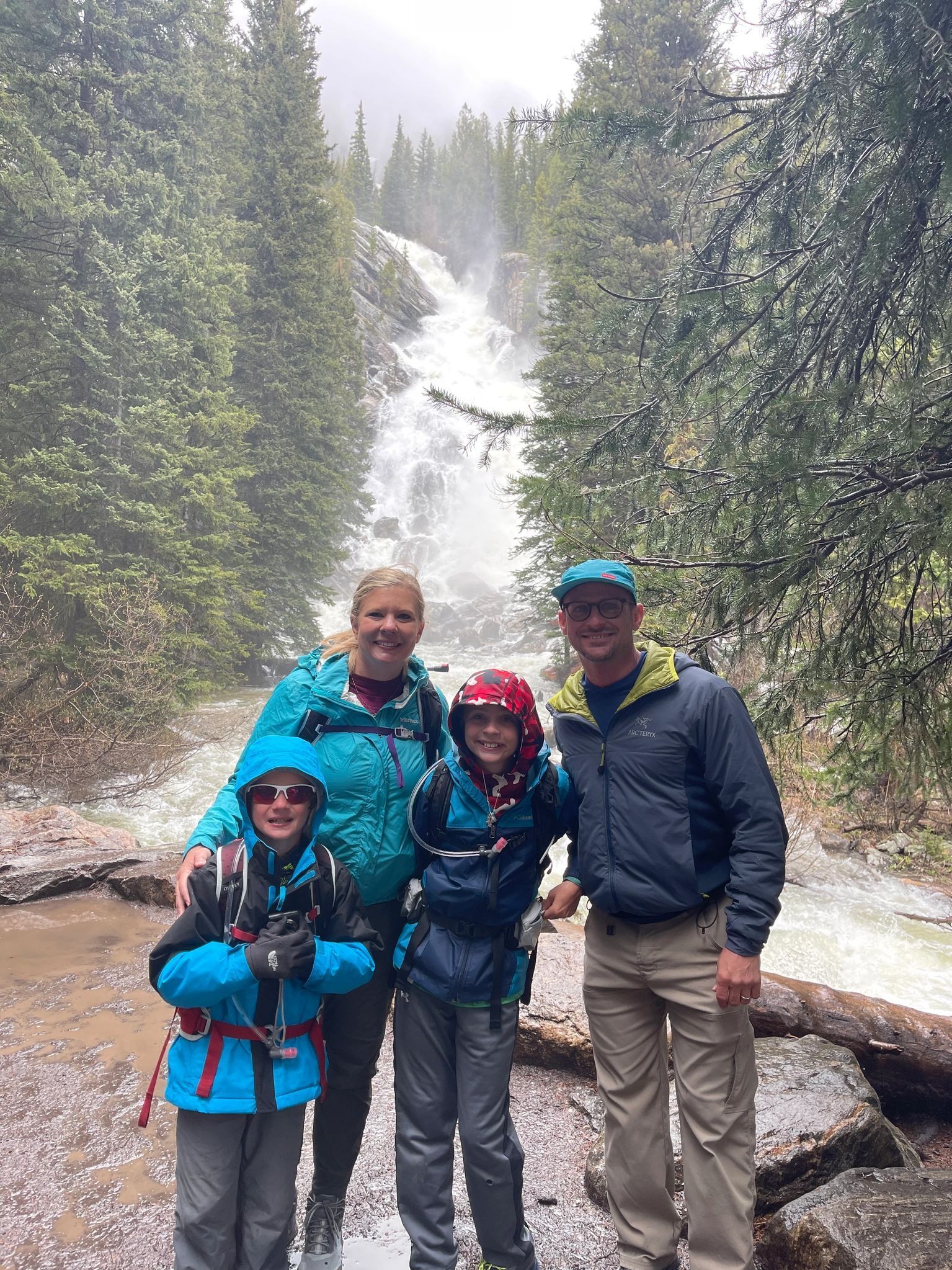 A family is standing in front of a waterfall in the woods.