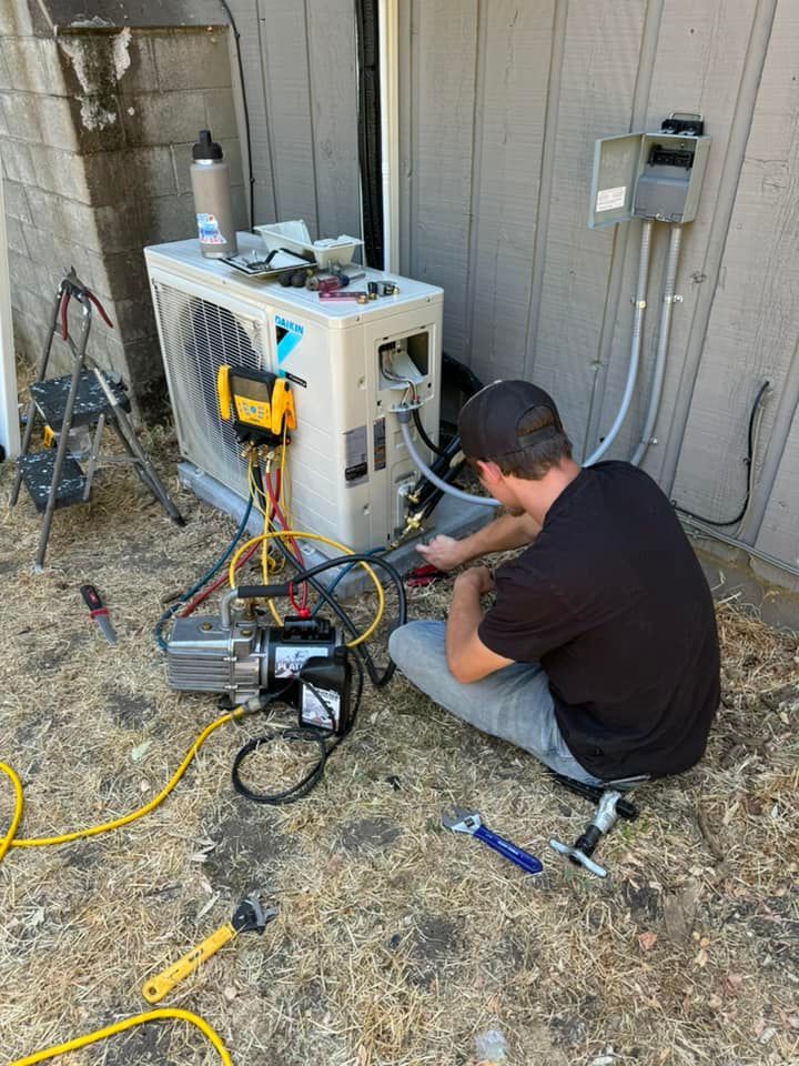 A man is sitting on the ground working on an air conditioner.