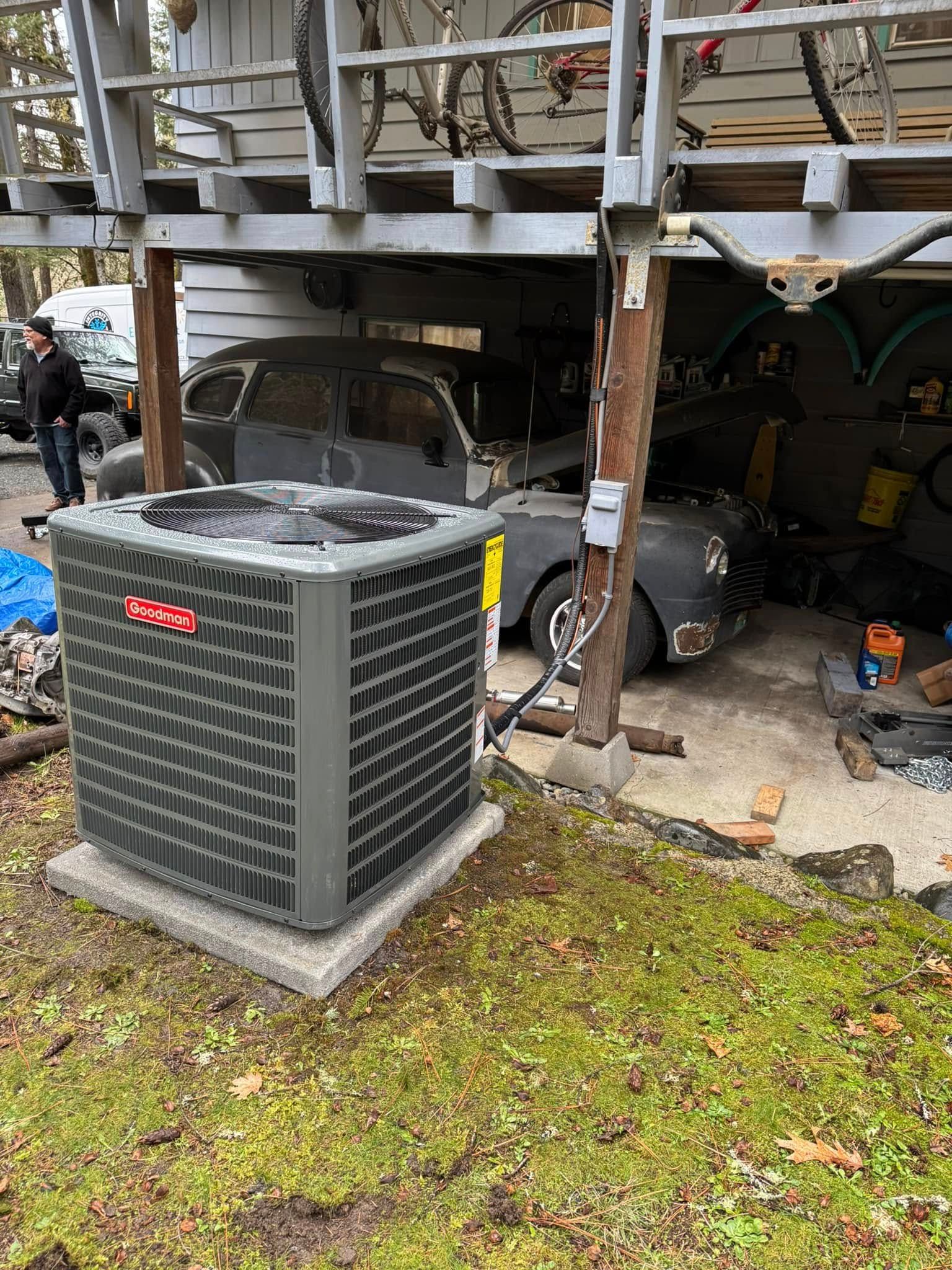 A large air conditioner is sitting in front of a garage under a house.