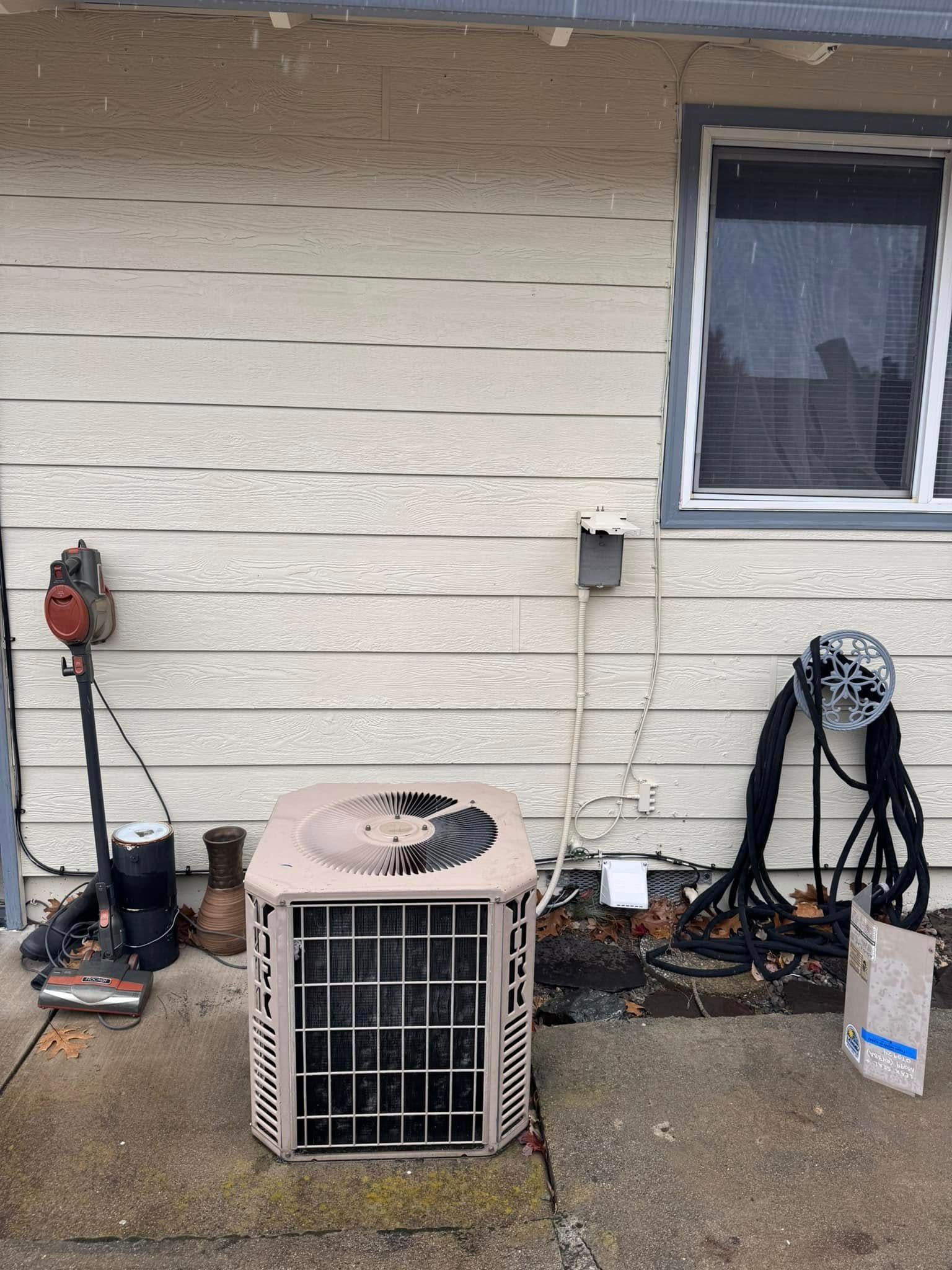An air conditioner is sitting outside of a house next to a window.