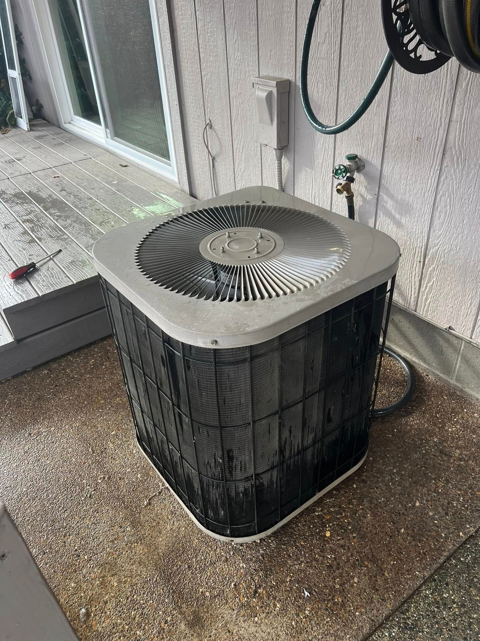 A black air conditioner is sitting on a patio next to a hose.