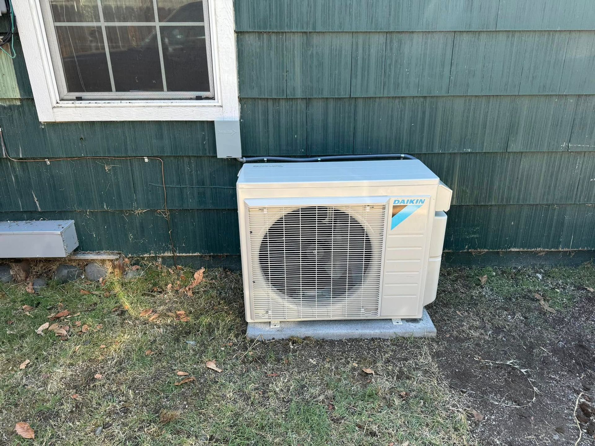 An air conditioner is sitting on the side of a house next to a window.