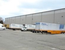 Truck trailers and a truck parked outside a large warehouse building.