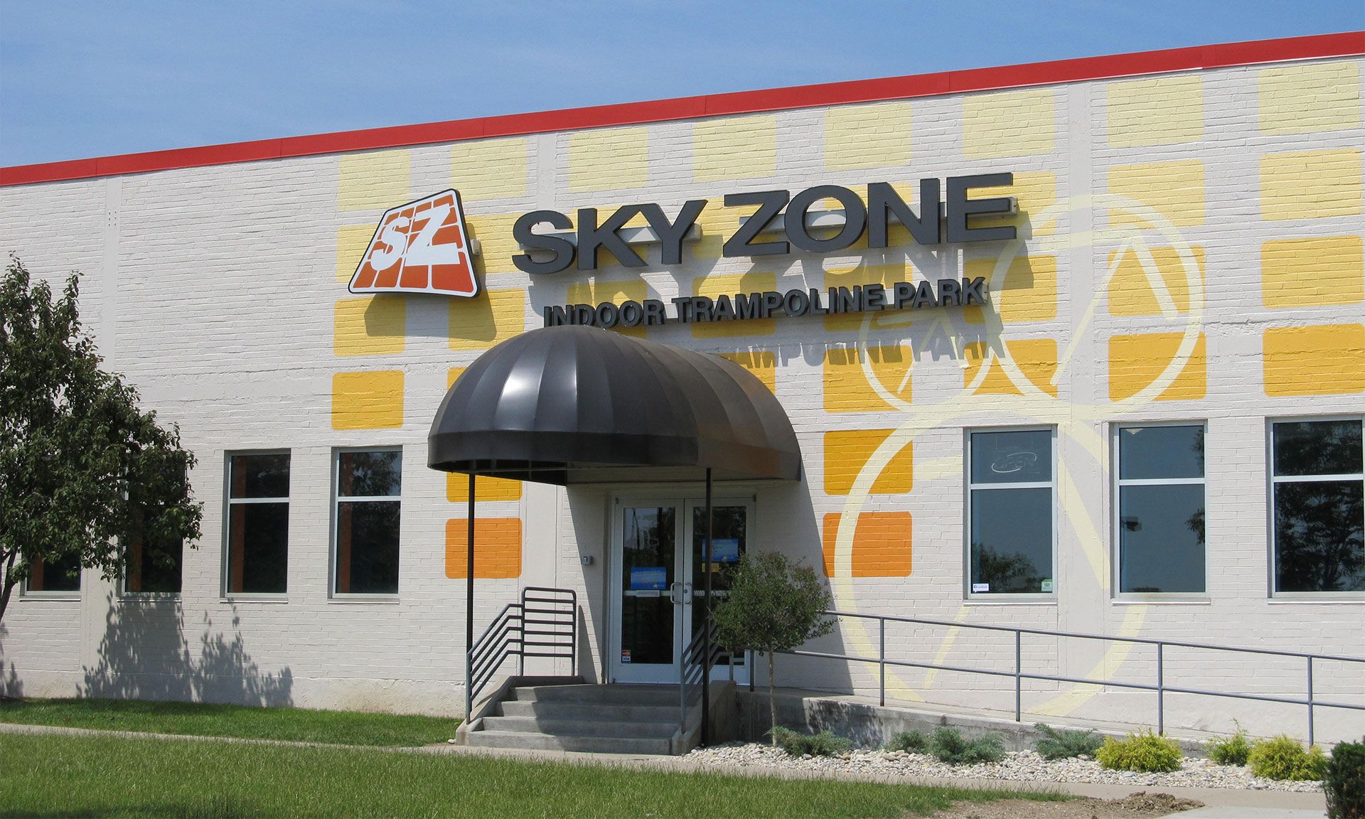 Sky Zone indoor trampoline park entrance, beige brick building with red and yellow accents.