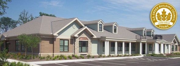 A light green building with a beige roof and columns, with a parking lot in front, and a gold emblem on the right.