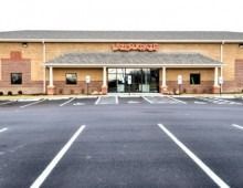 Exterior of a strip mall with a storefront. Tan brick, black asphalt, and a sign.