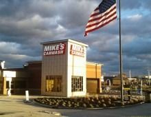 Mike's Carwash building with American flag waving against a cloudy sky.