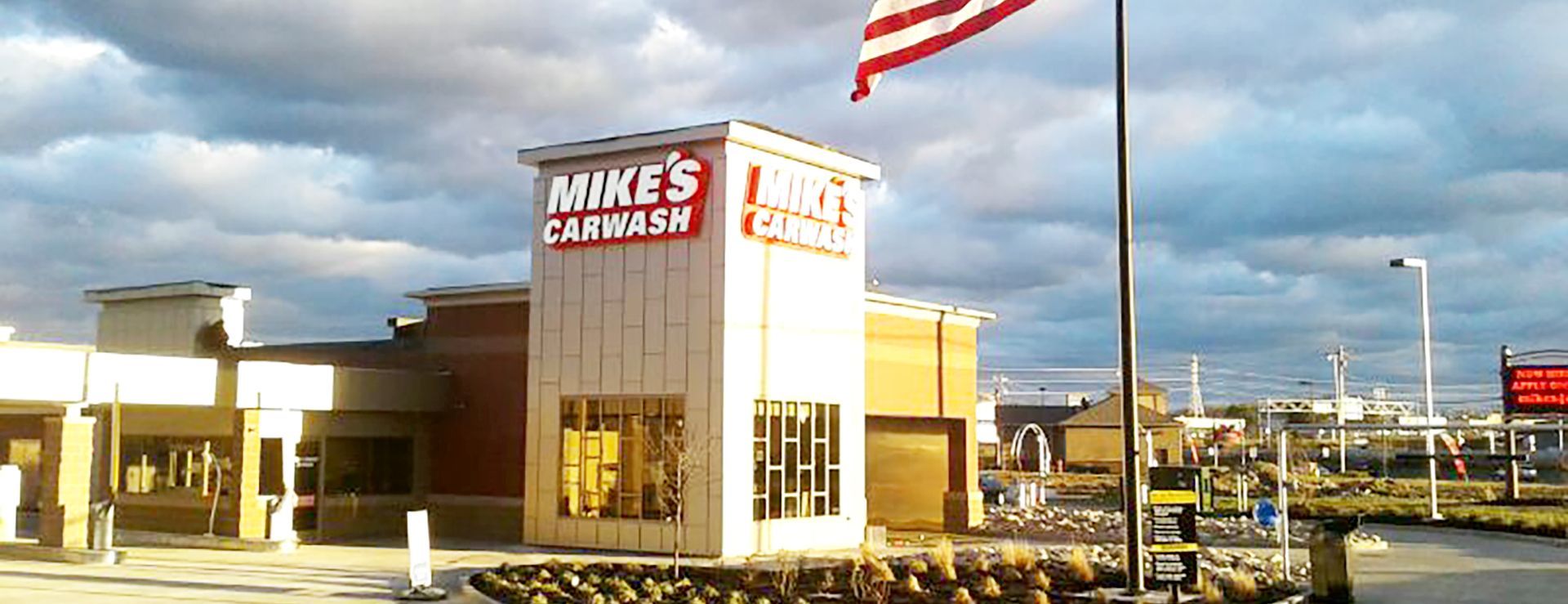 Exterior view of Mike's Carwash with an American flag, cloudy sky, and drive-through lanes.